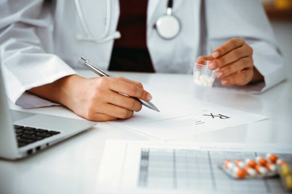 psychiatrist holding a cup with pills and filling out a prescription